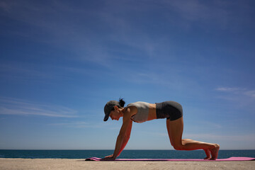 Brunette Woman Performing Isometric Exercises on Pink Exercise Mat by the Sea