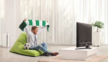 Man at home cheering with a scarf sitting and watching football