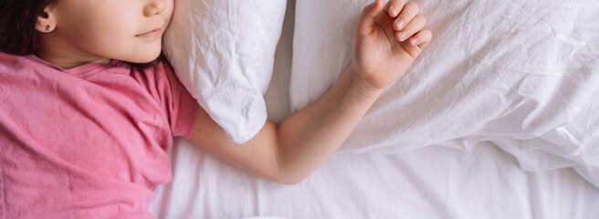 Little girl in pink pajamas sleeps in white bed linen.