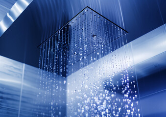 A high-resolution photograph of an advanced, futuristic and minimalist modern stainless steel bathroom with a wall mounted rainhead, in which water is falling down from the ceiling to form delicate dr
