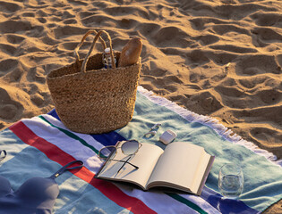 Jute beach bag, wireless headphones, notepad and sunglasses on the striped towel on the sand. Summer vacation lifestyle concept