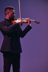 Elegant musician in black suit performing on violin under purple stage lights with artistic...