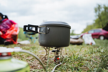 A pot is cooking on a gas stove in the grass field under the cloudy sky