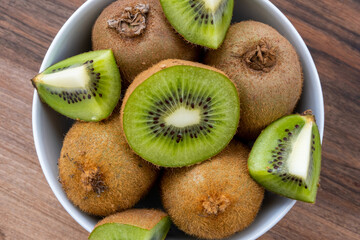 Top view of whole and sliced kiwi fruit in white bowl