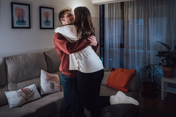 Young adult man and woman couple hugging in living room. Real life people at home
