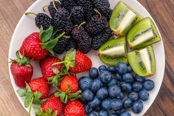 Closeup top view of blueberries, strawberries, kiwi and black mulberries on wooden table