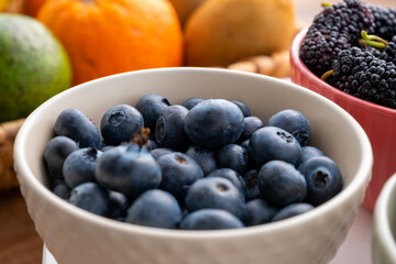 Closeup view of blueberries in bowl. Orange, kiwi and avocado in fruit basket.