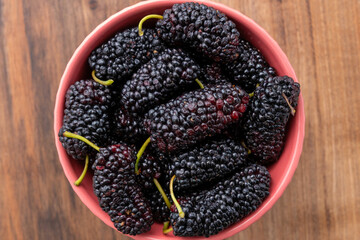 Top view of black mulberries in bowl on wooden table