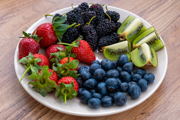 Closeup view of blueberries, strawberries, kiwi and black mulberries on wooden table