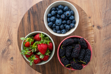 Top view of blueberries, strawberries and black mulberries on wooden table