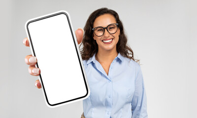 Businesswoman is seen holding a modern cell phone in her hand. The phones screen is blank, showing...