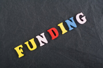 FUNDING word on black board background composed from colorful abc alphabet block wooden letters, copy space for ad text. Learning english concept.