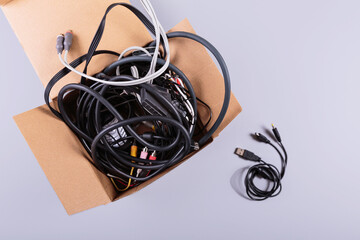 Cardboard box filled with old cables, wires, and button mobile phones against a gray background,...