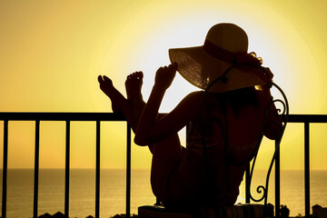 Silhouette of a girl on a chair in the loggia balcony background. A happy woman with a hat on vacation while traveling. - obrazy, fototapety, plakaty