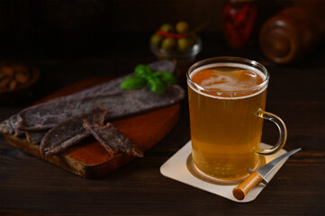 glass with beer and meat snacks nearby on a wooden background