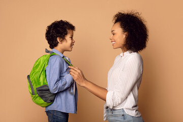 A joyful African American mother carefully fixes her sons backpack straps as they share a moment of...