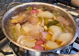 Chicken stock boiling in an oval pot on a gas stove