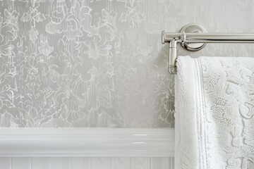 Elegant white towel hangs on a shiny silver towel rack against a beautifully patterned gray wallpaper, showcasing a luxurious and well-organized bathroom setting.