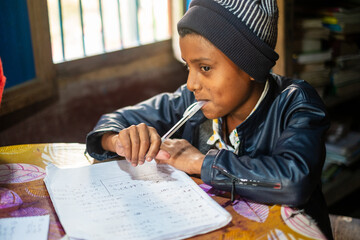 South asian school going boy solving mathematics homework , indoor image of a student writing in a...