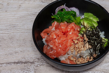 Salmon and seaweed poke in a black bowl on wooden table