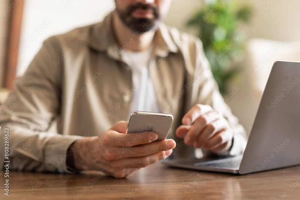 Aufkleber Cropped of man is sitting at a table while actively using a cell phone. He appears engaged with the device, possibly texting, browsing, or talking on the phone.