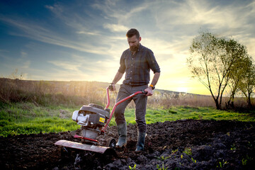 organic farming man ploughs the ground at sunset with a tiller preparing the soil for sowing