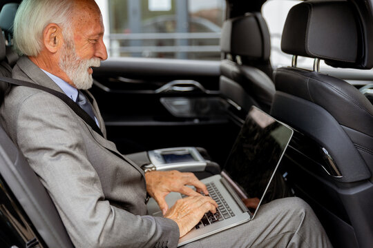 Elderly businessman working on laptop while parked in his car on a busy day