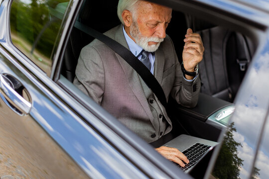 Senior businessman working on laptop while riding in backseat of car