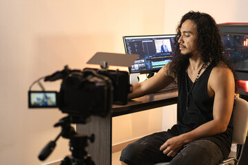 Professional Filmmaking Setup. A long-haired content creator immersed in his studio, recording videos with his phone mounted on a tripod. Cameras, lights, and a computer are part of his setup