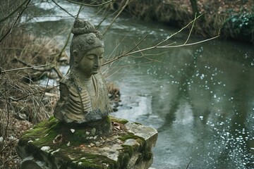 Tranquil buddha statue sits in meditative pose beside a gently flowing stream, surrounded by nature