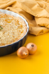 Homemade onion cake on the yellow background. Traditional quiche pie with steamed onions, cheese and bacon