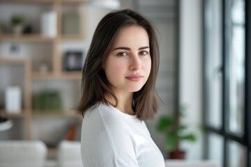 Obraz premium Portrait of a calm young woman with a gentle smile, posing in a bright, contemporary living room environment with blurred background emphasizing her serene expression