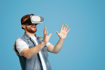 Happy young male touching invisible subject in virtual glasses and enjoying the moment, blue...