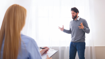 Emotional bearded man standing next to window at counselor office, gesturing while talking,...