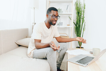 Smiling African American Freelancer Working on Laptop on a Modern Sofa in a Cozy Living Room