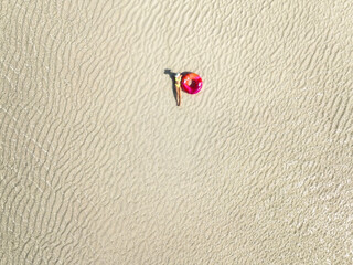 Aerial view of lying sporty slim woman with swimming ring, sandy beach in low tide at sunrise in...