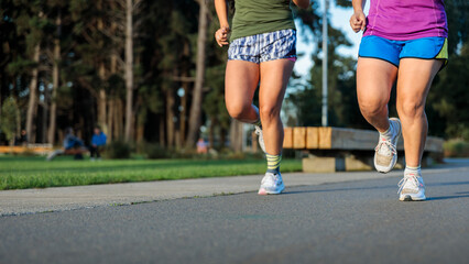 Low angle view of the legs from unrecognizable women jogging and enjoying vitality in the park at afternoon. Copy space