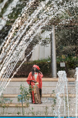 Middle-aged woman in traditional costume standing next to a fountain in a park. lifestyle tradition