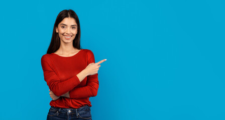 A woman wearing a red shirt is pointing at an unidentified object or direction. Her gesture is...