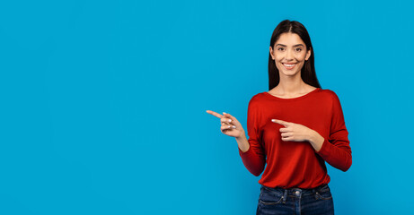 A woman wearing a red sweater is pointing at an unseen object off-camera, engaged and focused on...