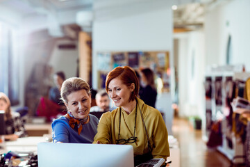 Two female designers using computer for project in a busy office environment