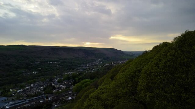 Aerial shot emerging from behind trees on a Welsh Valley mountainside to reveal an evening sky