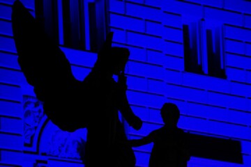 Schatten einer historischen Engel Statue auf der Schlossbrücke, Berlin gegen einen blauen Neon Hintergrund bei Nacht