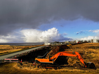 Excavator with a bucket, construction site on the shores of the Atlantic Ocean, Iceland. A rock...