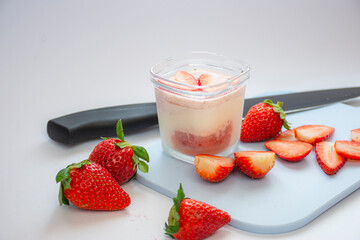 A homemade natural yogurt with fresh red strawberries on a cutting board and a knife