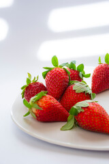 Several fresh red strawberries on a plate on a white background