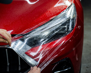 The master applies vinyl film to the headlight of a red car. 