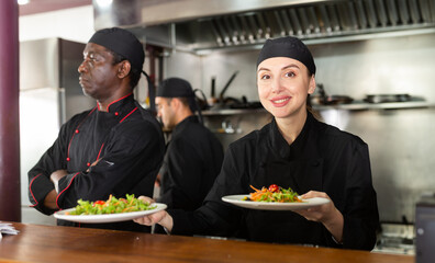 Female chef puts in black uniform ready meals on shelves in modern restaurant