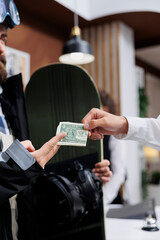 Close-up of male traveler with snowboard giving tip money to employee at counter of luxury winter...