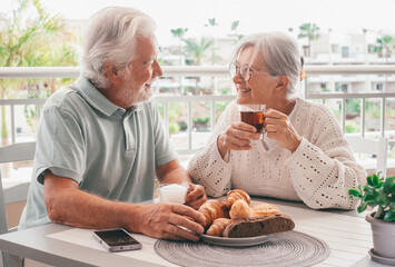 Smiling bonding senior retired couple looking into each other's eyes enjoy breakfast together sitting outdoors on home terrace. Serene retirement lifestyle concept